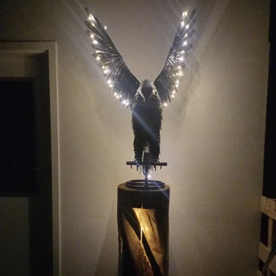 Stammholzlampe mit Adler Skulptur eines Vogels mit leuchtenden Flügeln auf einem Holzsockel.